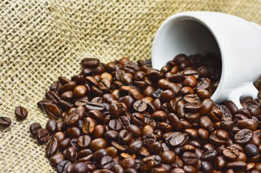 Yakın çekim fotoğraf bulanık arka plan ve metin için yer ile jüt çanta beyaz porselen fincan ile kavrulmuş siyah kahve tanelerinin