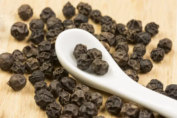 Close-up foto de natureza morta com bolas de pimenta preta com colher de porcelana branca no tapete de madeira — Fotografia de Stock