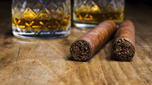 Dwa kubańskie cygara z dwie szklanki whisky na stary, drewniany stół z niewyraźne tło — Zdjęcie stockowe