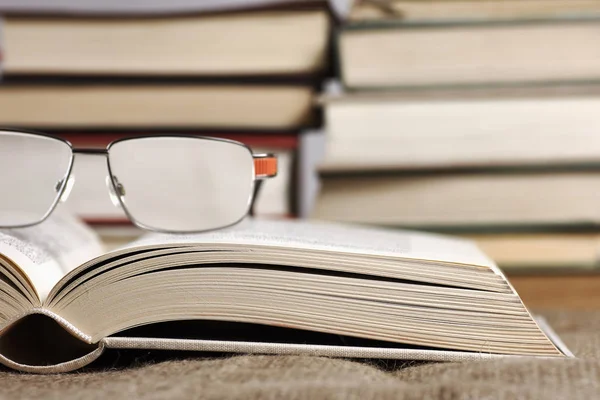 Otevřená kniha s brýlemi ležící na rohož juta s bokeh — Stock fotografie