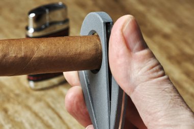 Bir kesici ve bulanık bir çakmak arka planda tutan bir erkek el ile Küba purosu