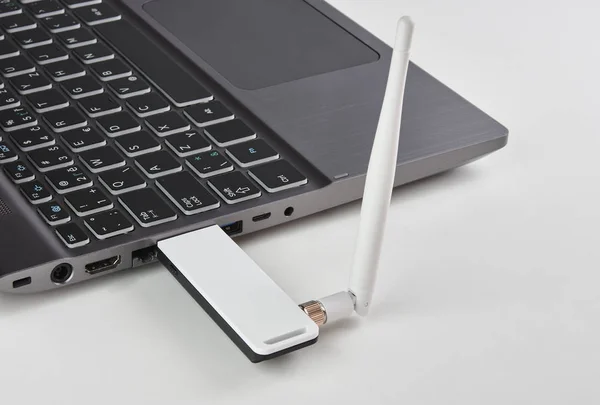 Серебряный ноутбук с USB-модемом, подключенный к антенне, на белом столе — стоковое фото
