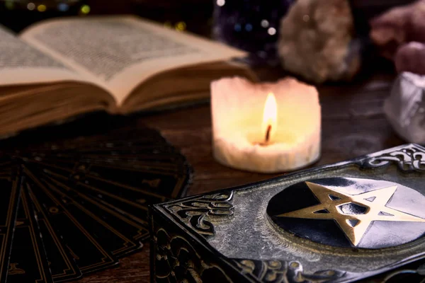 Bodegón con vela encendida en la mesa de madera vieja, tarjeta de adivino negro, libro mágico y caja con pentagrama. Adecuado para magia o esotérico . — Foto de Stock