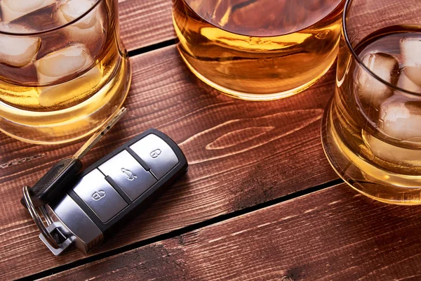 Modern car keys on wooden table top in bar. Glass and bottle of