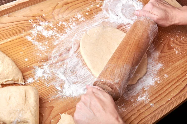 Kneaded dough on a rolling plate with spilled wheat flour. Hands