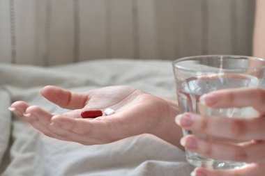 Genç bir kadının ellerine yakından bak. Yatakta elinde tablet, hap ve bir bardak su tutan bir kız. Mesaj için yeri olan bir ağrı kesici. Bulanık arkaplan.