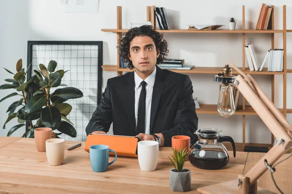 Geschäftsmann mit Tablet und Kaffeetassen am Arbeitsplatz — kostenloses Stockfoto