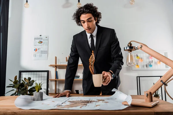 Businessman pouring coffee on blueprints — Stock Photo, Image