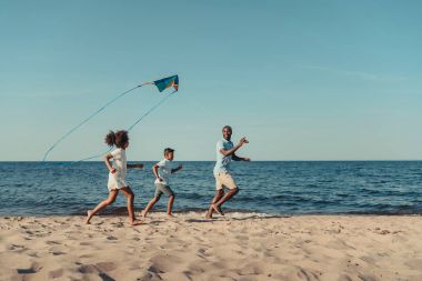 father and kids playing with kite on beach clipart