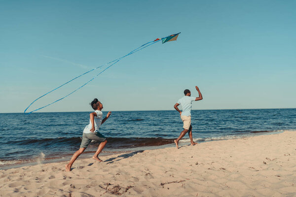 Отец и сын играют с воздушным змеем на пляже
