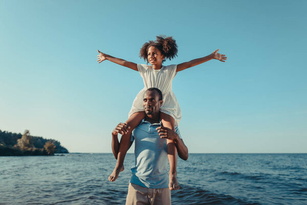african american father carrying daughter on beach
