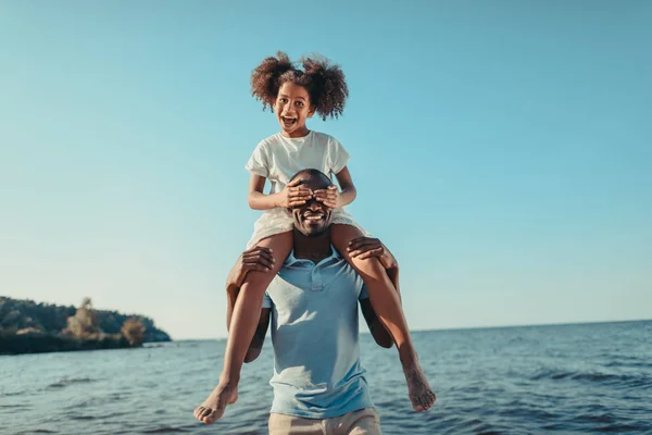 African american father carrying daughter on beach — Stock Photo, Image