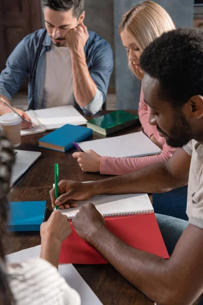 Multiethnic students writing in copybooks — Stock Photo, Image