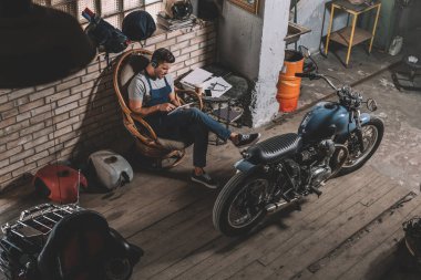 mechanic in repair shop with motorbike clipart