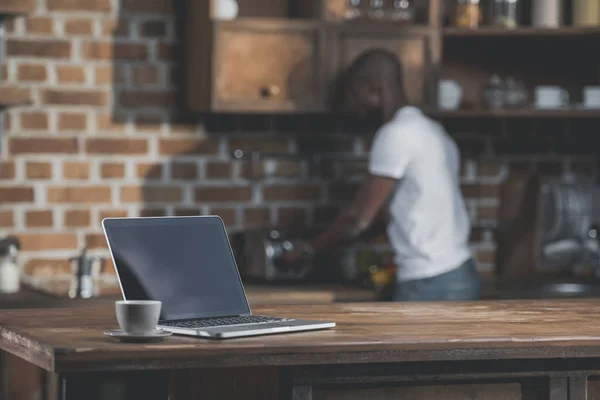 Laptop and cup of coffee in kitchen — Stock Photo