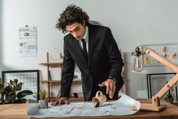 Businessman pouring coffee on blueprints — Stock Photo