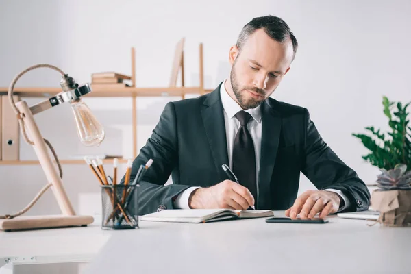 Nachdenklicher Geschäftsmann schreibt in Notizbuch — Stockfoto