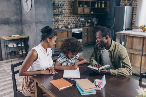 Little girl writing at notebook with parents — Stock Photo