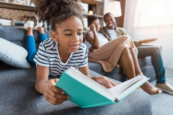 Menina deitada no sofá com livro — Fotografia de Stock