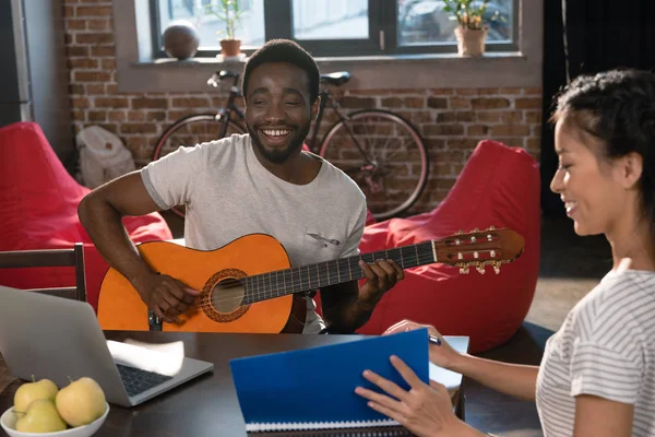 Chica estudiando mientras estudiante jugando guitarra - foto de stock