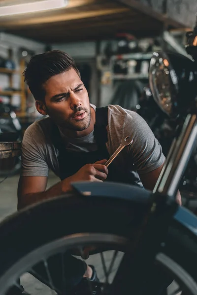 Mechanic with wrench repairing motorbike — Stock Photo