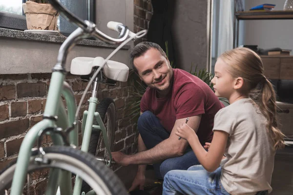 Батько ремонтує дочки велосипед — стокове фото