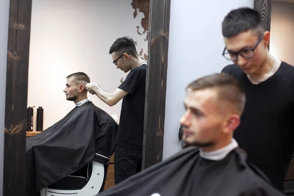 young guy makes a short haircut in a barbershop, a barber Kazakh cuts a man with a trimmer, reflection in the mirror