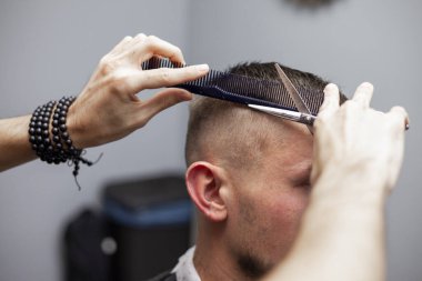 Yakışıklı adam kuaförde saç tıraşı oluyor, Kazak kuaför elle makas ve kısa saç kesimi yapıyor.