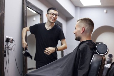 Kazak genç kuaför kuaförde çalışıyor, adam berber dükkanında oturuyor ve kısa saç kesimi yapıyor.