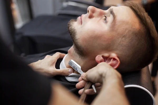 handsome guy cut his beard with a razor, shaving a short beard in a barbershop, close-up