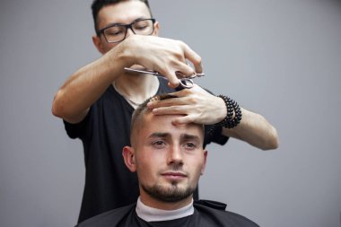 Bir adam berber dükkanında saçını kestirir, genç bir Kazak berber manuel olarak makas ve tarak kullanır, usta kuaförde kısa kestirme yapar.