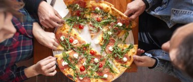 Bir grup öğrenci İtalyan pizzası yer, eller bir restoranda pizza yer.