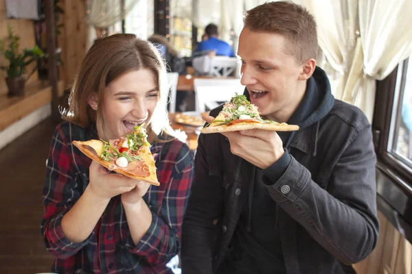 カップルはピザ屋に座ってピザを食べ男と女はファーストフードを食べ笑顔でレストランでリラックスします — ストック写真