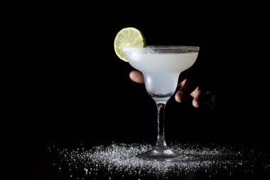 Barmen limonlu klasik margarita servis ediyor, elinde siyah bir arka planda kokteyl tutuyor.