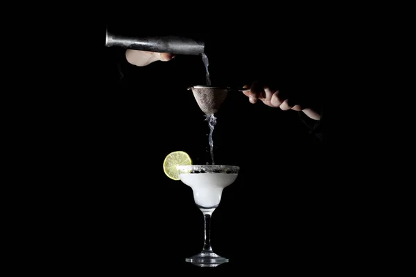 Barman está preparando um clássico margarita, ele está derramando um coquetel em um copo em um fundo preto — Fotografia de Stock