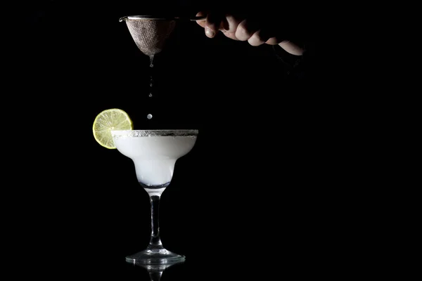 Barman está preparando um clássico margarita, ele está derramando um coquetel em um copo em um fundo preto — Fotografia de Stock
