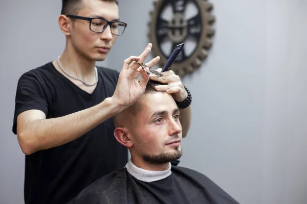 handsome guy get a haircut at the hairdresser, Kazakh hairdresser cuts manually with scissors and a comb, short haircut close-up