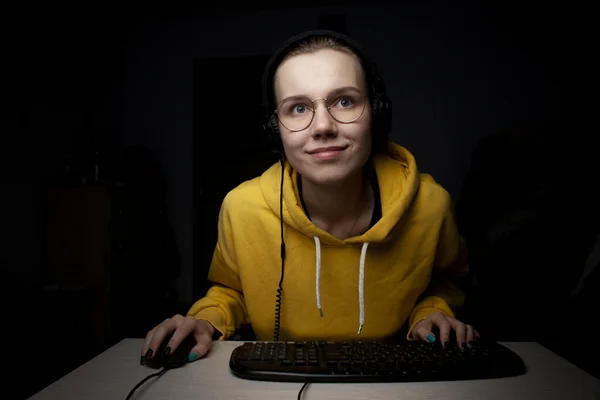 女孩晚上在家里的电脑上玩电子游戏，一个学生把注意力集中在游戏上 — 图库照片