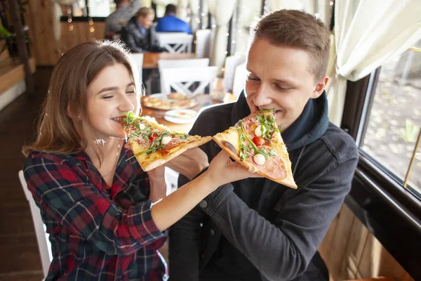 Pareja se sienta en una pizzería y come pizza, un chico y una chica cenan comida rápida, sonríen y se relajan en un restaurante — Foto de Stock