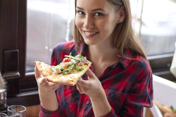 Jong meisje eten een stuk pizza binnen, meisje student geeft pizza, close-up — Stockfoto