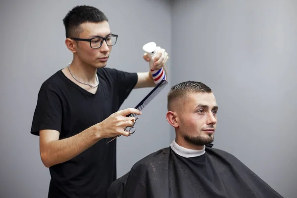 Kazakh barber gives the client a short haircut with scissors and a comb, hairdresser a student does a hairstyle
