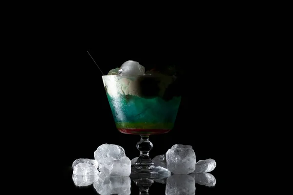 Coquetel multicolorido com gelo e espuma em um copo em um fundo preto — Fotografia de Stock