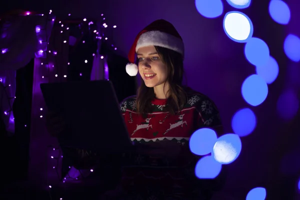 Noel kıyafetleri içindeki kız geceleri evde dizüstü bilgisayarla oturuyor, yalnız bir kadın tatille internetten tanışıyor, Noel 'de bilgisayar kullanıyor. — Stok fotoğraf