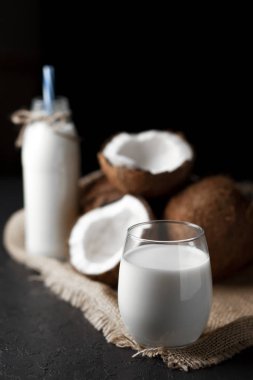 Koyu bir arka planda bardakta hindistan cevizi sütü, hindistan cevizinden kozmetik kremi ve kumaş.