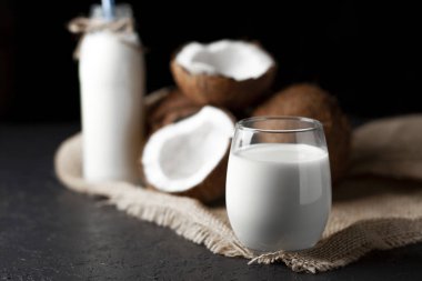 Koyu bir arka planda bardakta hindistan cevizi sütü, hindistan cevizinden kozmetik kremi ve kumaş.
