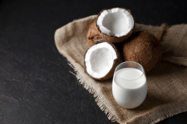 Koyu bir arka planda bardakta hindistan cevizi sütü, hindistan cevizinden kozmetik kremi ve kumaş.