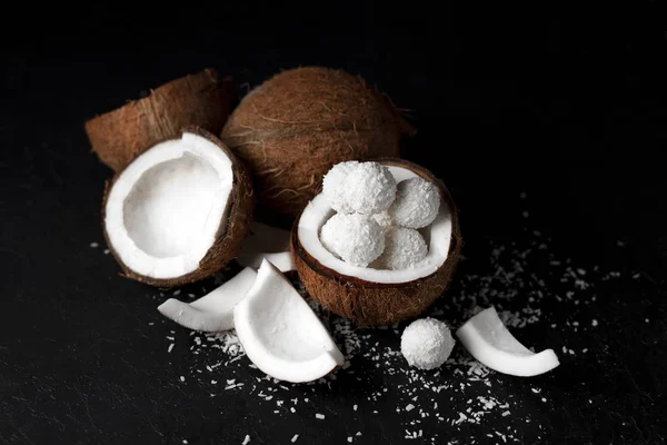 Doces de leite de coco cozidos em um fundo preto escuro, ingredientes para uma sobremesa com cocos, um produto doce com flocos de coco — Fotografia de Stock