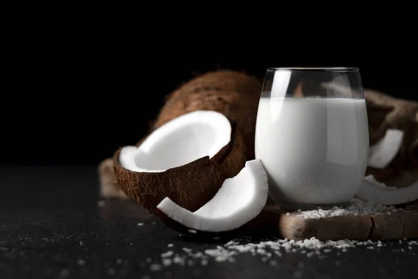 Latte di cocco fresco in un bicchiere su sfondo scuro, crema cosmetica al cocco, frullato con fette di cocco — Foto Stock
