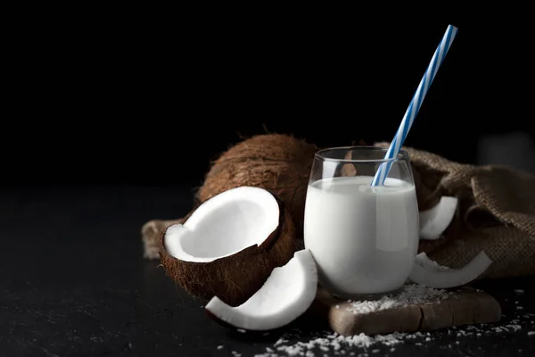 Latte di cocco fresco in un bicchiere su sfondo scuro, crema cosmetica al cocco, frullato con fette di cocco — Foto Stock