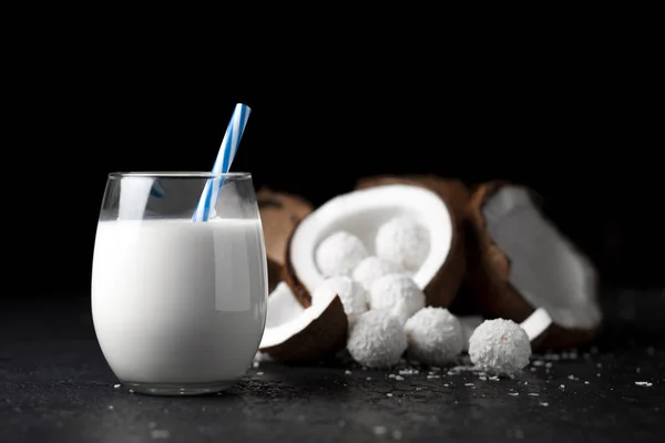 Latte di cocco bianco in un bicchiere su fondo nero scuro, dolci con scaglie di cocco, prodotti da cucina — Foto Stock